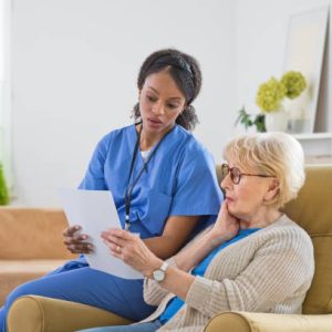 Female home caregiver supporting senior woman in her house, reviewing documents together. They are worried.